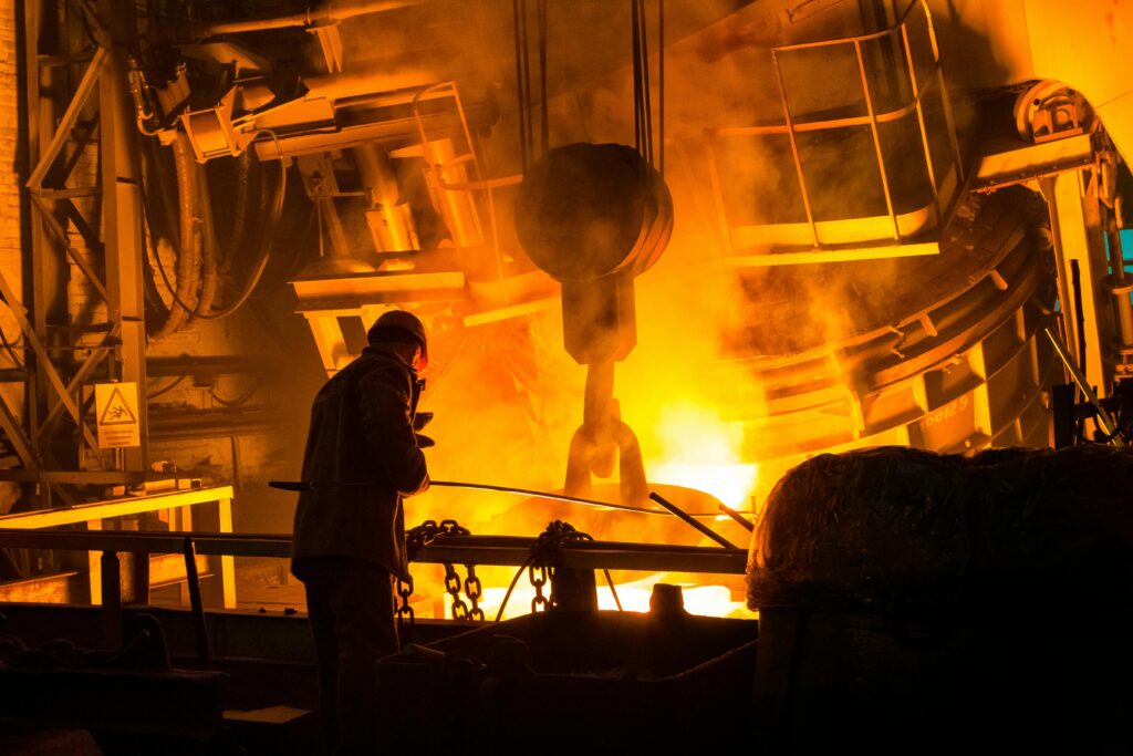 A worker operates machinery in a factory with molten metal and intense flames.